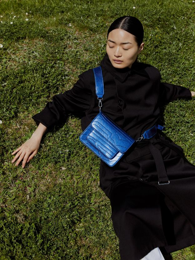 A woman laying in a grass and wearing a blue HVISK bag