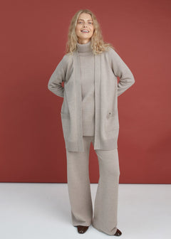 Woman wearing a beige knit outfit against a red background