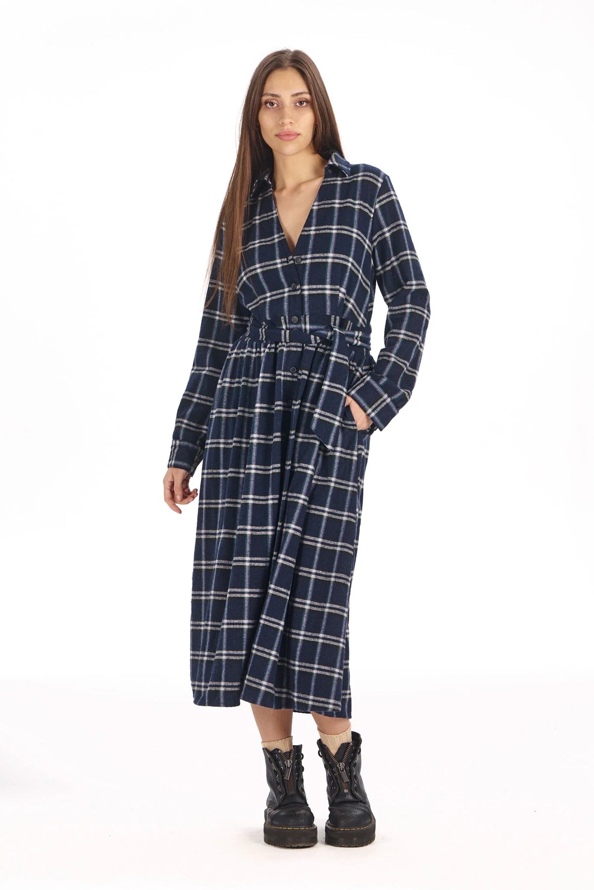 A woman modeling a navy blue and white plaid midi dress with a tie waist and black combat boots, photographed against a solid white background.