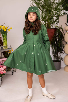Young girl wearing a green raincoat with white floral patterns in a room with plants and flowers.