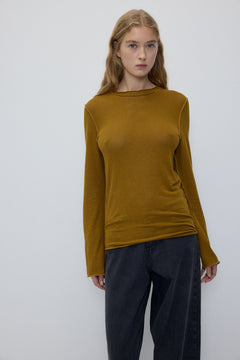 A woman modeling a ribbed long-sleeve knit top in a mustard yellow color, paired with dark gray wide-leg jeans, against a plain light gray studio background.