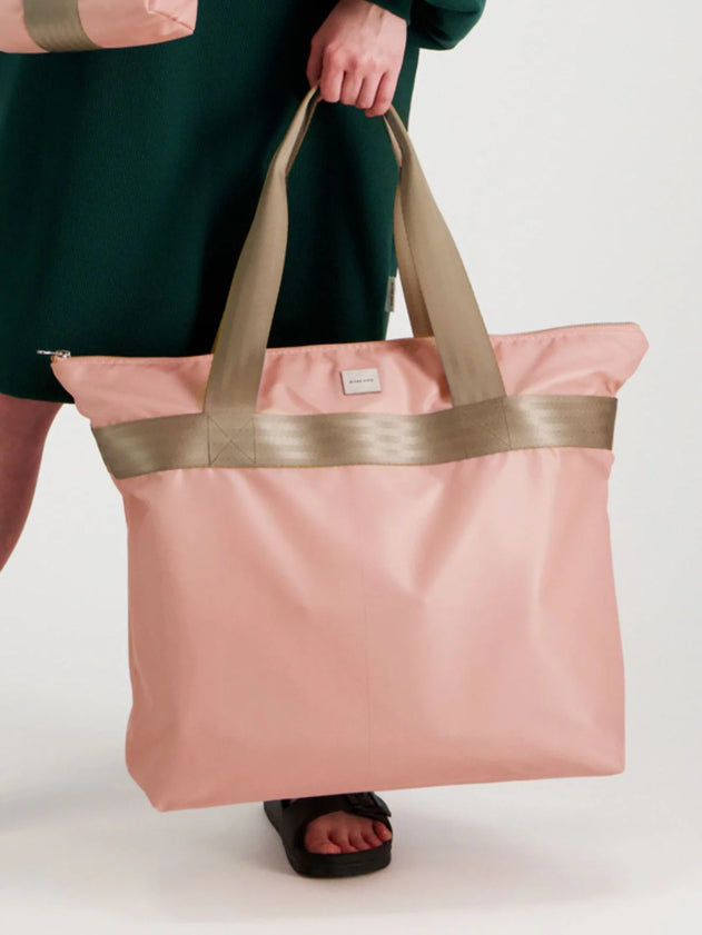 Person holding a pink tote bag with gold accents on a white background