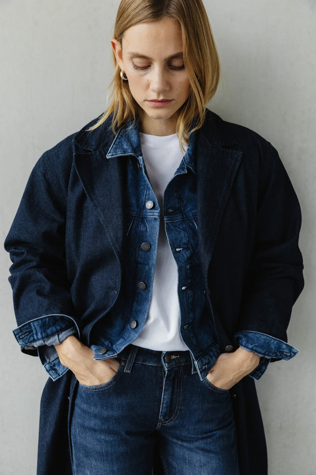 Person wearing a dark denim jacket and jeans against a plain background