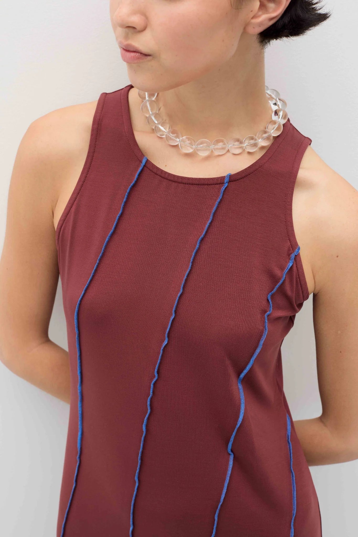 Person wearing a maroon sleeveless top with blue piping against a plain background