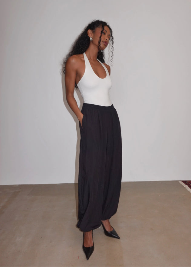 Woman wearing a white top and black pants against a plain background