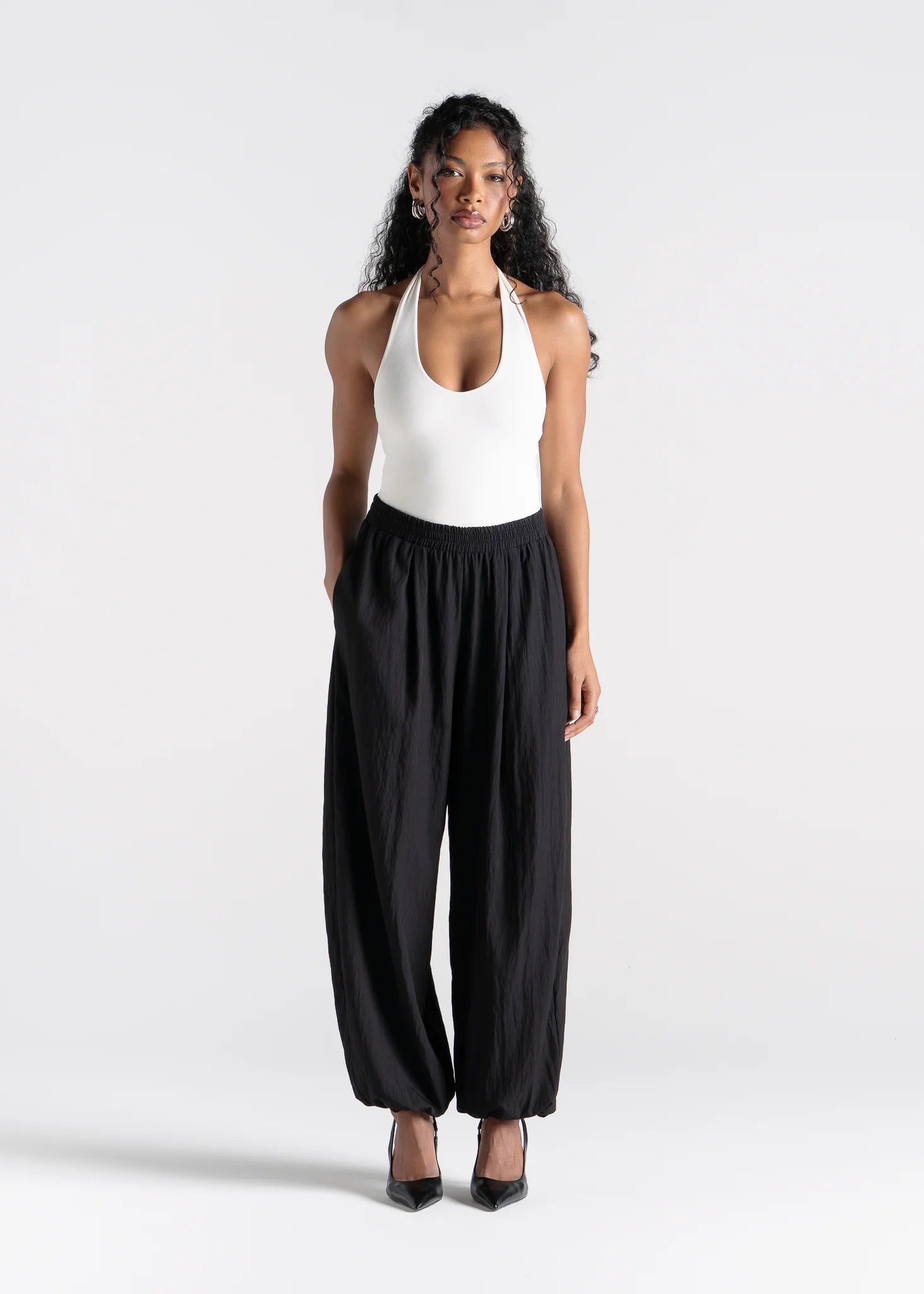 Woman wearing a white halter top and black wide-leg pants on a white background