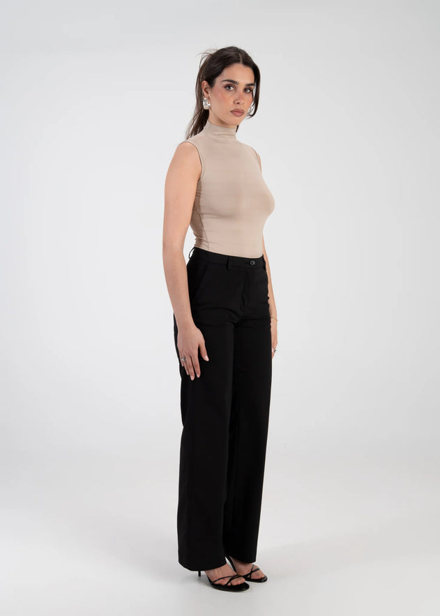 Woman wearing a beige sleeveless top and black high-waisted pants on a white background