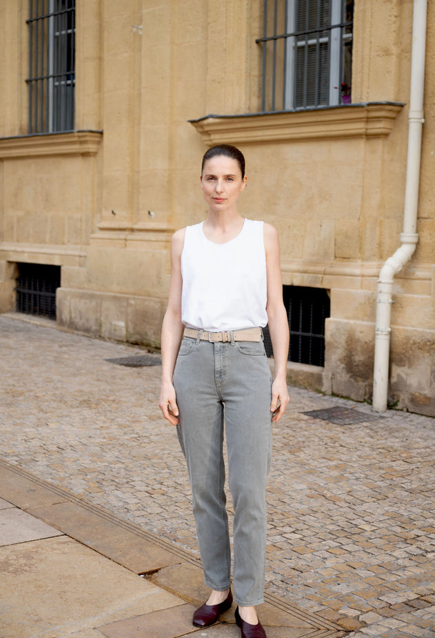 Woman in a white sleeveless top and gray pants standing on a street with a building in the background.