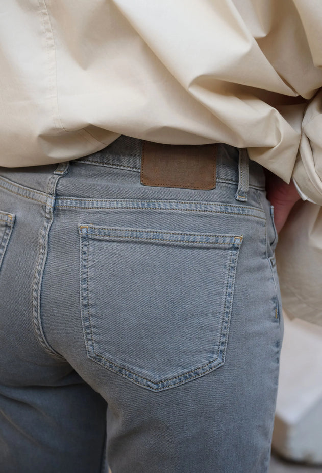 Person wearing a beige shirt and blue jeans with a neutral background
