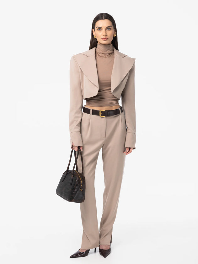 Woman wearing a beige suit with a black handbag on a white background
