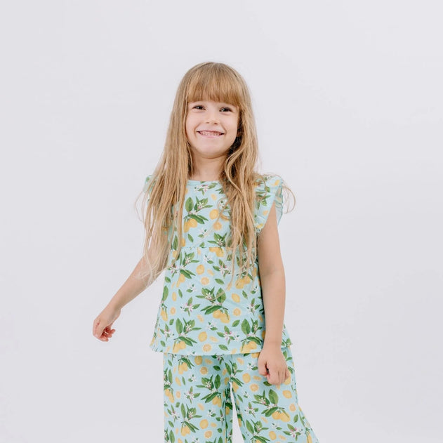 Child wearing a light blue pajama set with lemon print on a white background