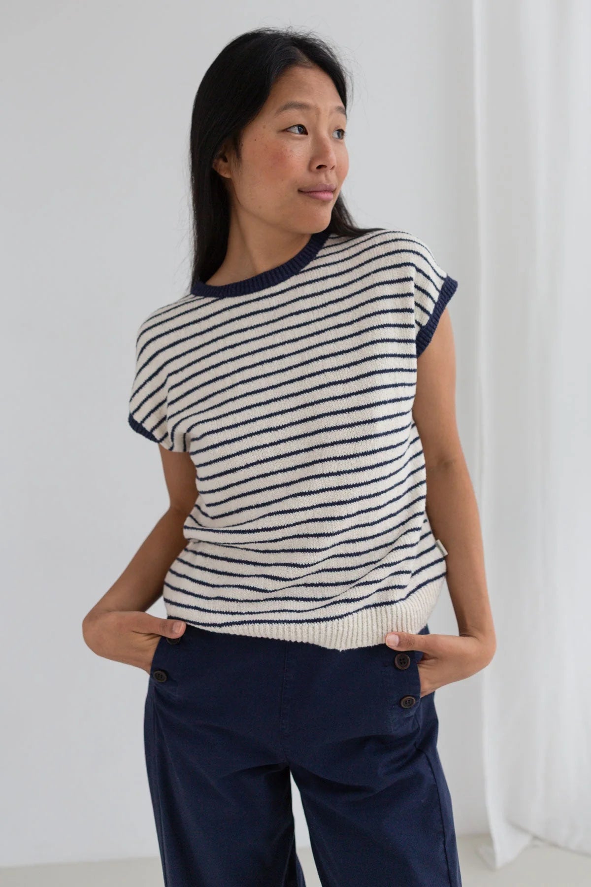 Woman wearing a black and white striped sweater with navy pants against a white background