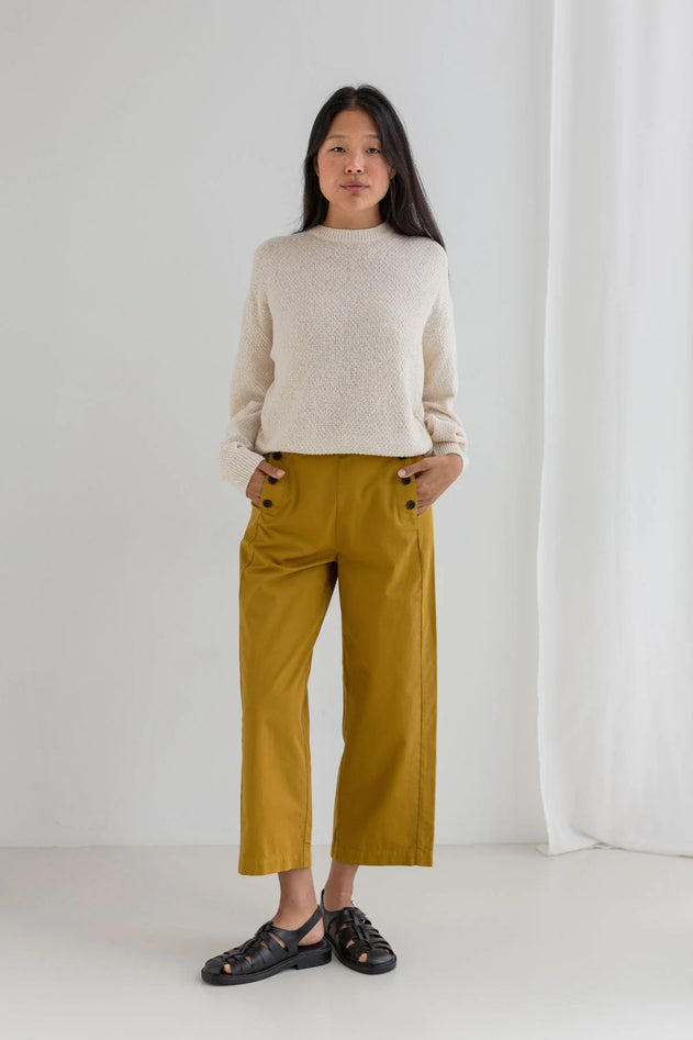 Woman wearing a beige sweater and mustard yellow pants against a white background