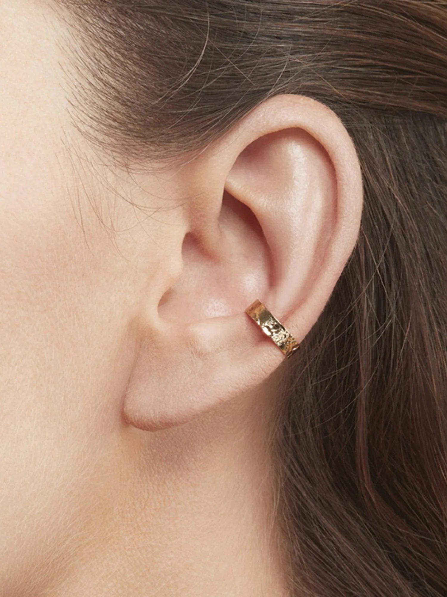 Close-up of an ear wearing a gold earring with hair partially covering the side.
