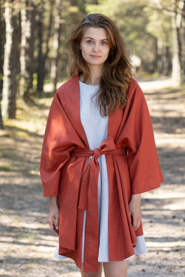 Woman wearing a red coat over a white dress in a forest setting