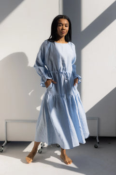 Woman wearing a light blue dress standing against a white wall with geometric shadows.