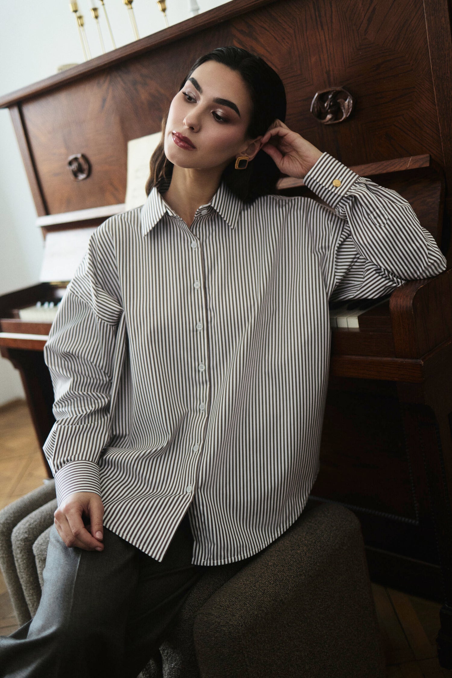 Woman wearing a striped shirt sitting in a room with wooden furniture.