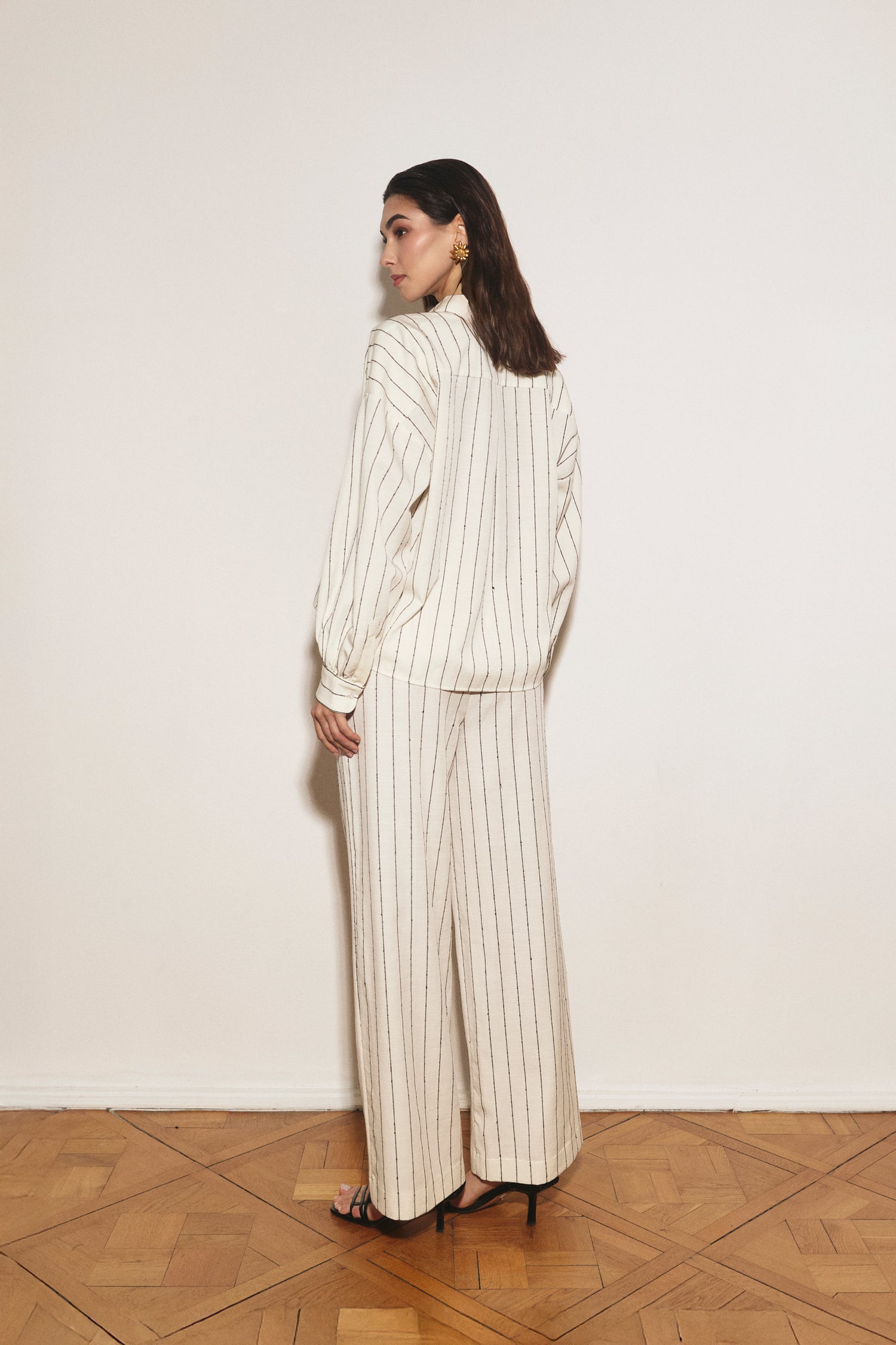 Person wearing a striped suit standing against a white wall.