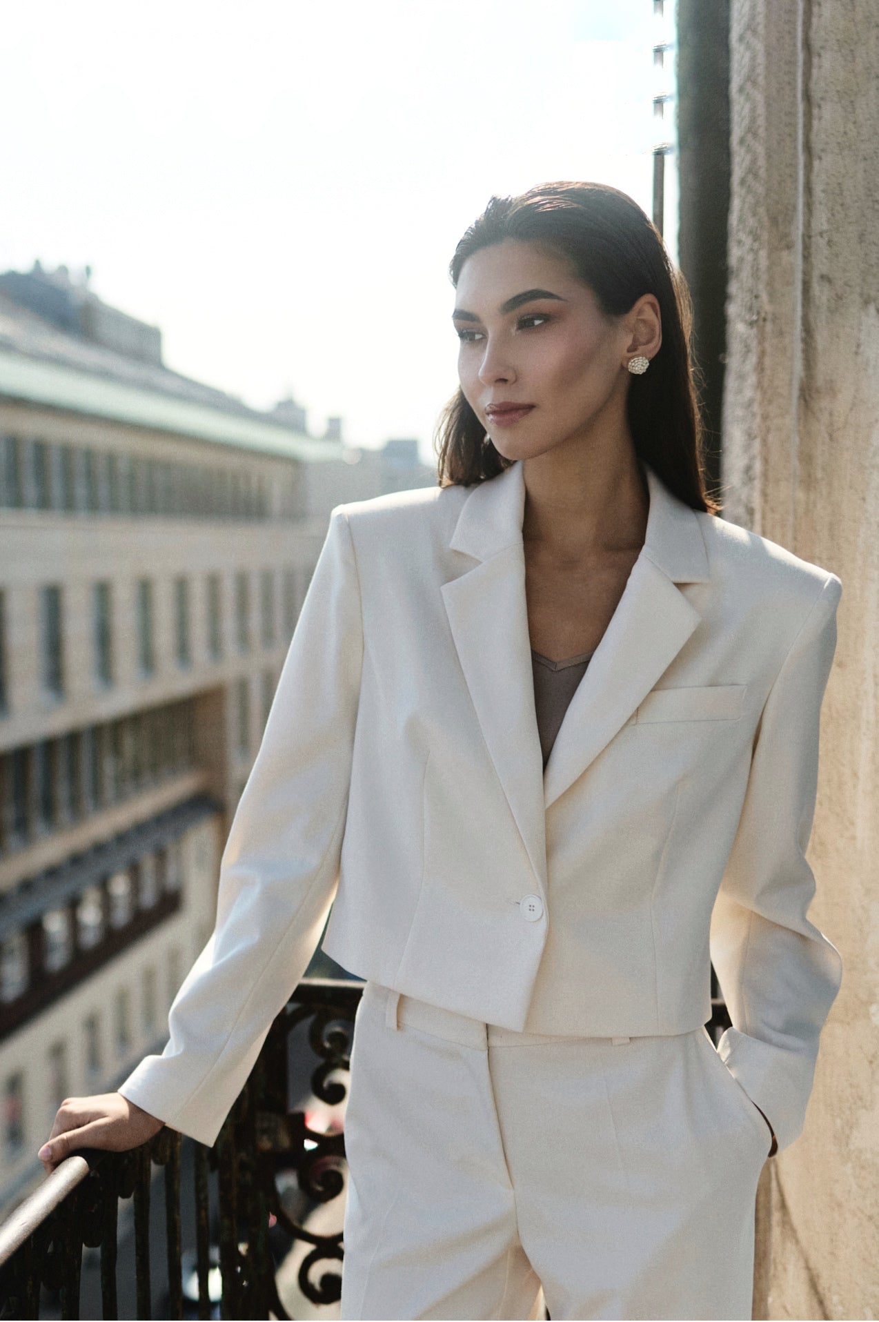 Woman in a white suit standing on a balcony with a cityscape background