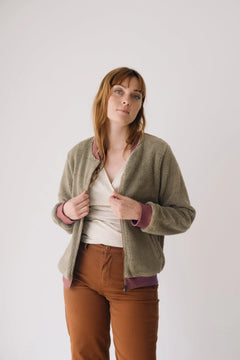 Woman wearing a green cardigan over a white shirt and brown pants on a plain background
