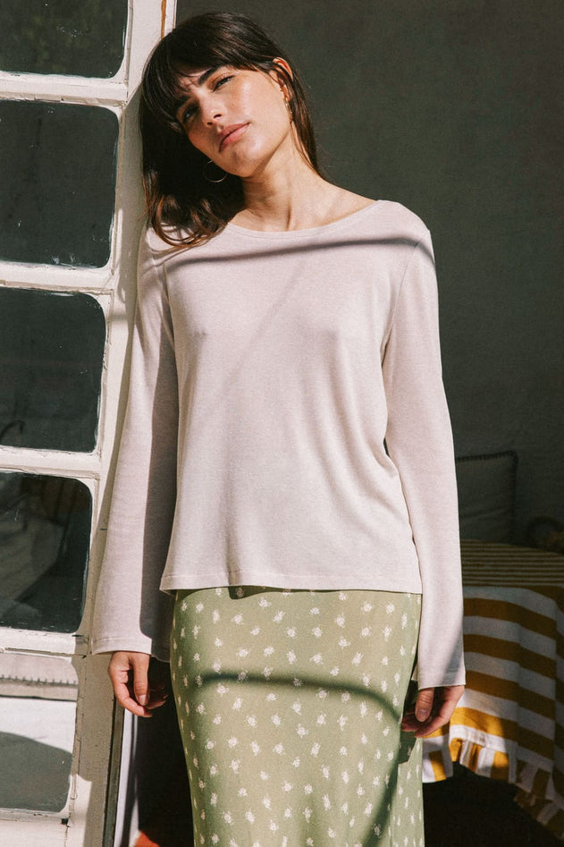 Woman wearing a light pink sweater and green polka dot pants standing against a textured wall.