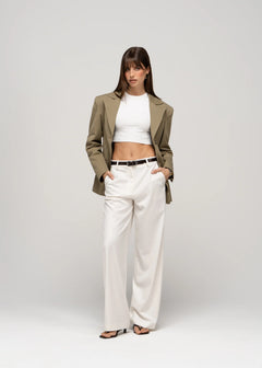 Woman wearing a green blazer, white top, and beige pants on a white background