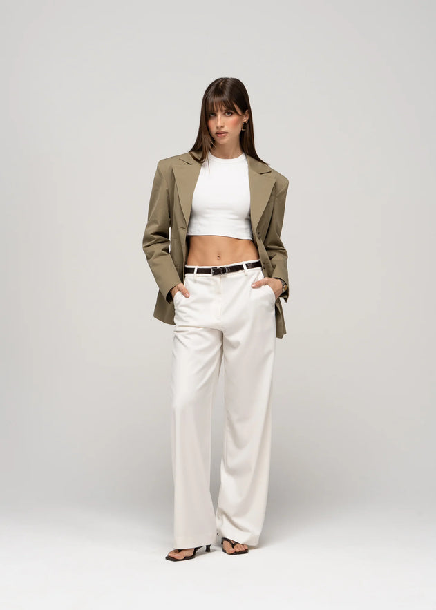 Woman wearing a green blazer, white top, and beige pants on a white background