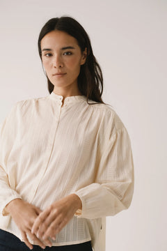 Woman wearing a light-colored blouse against a plain background