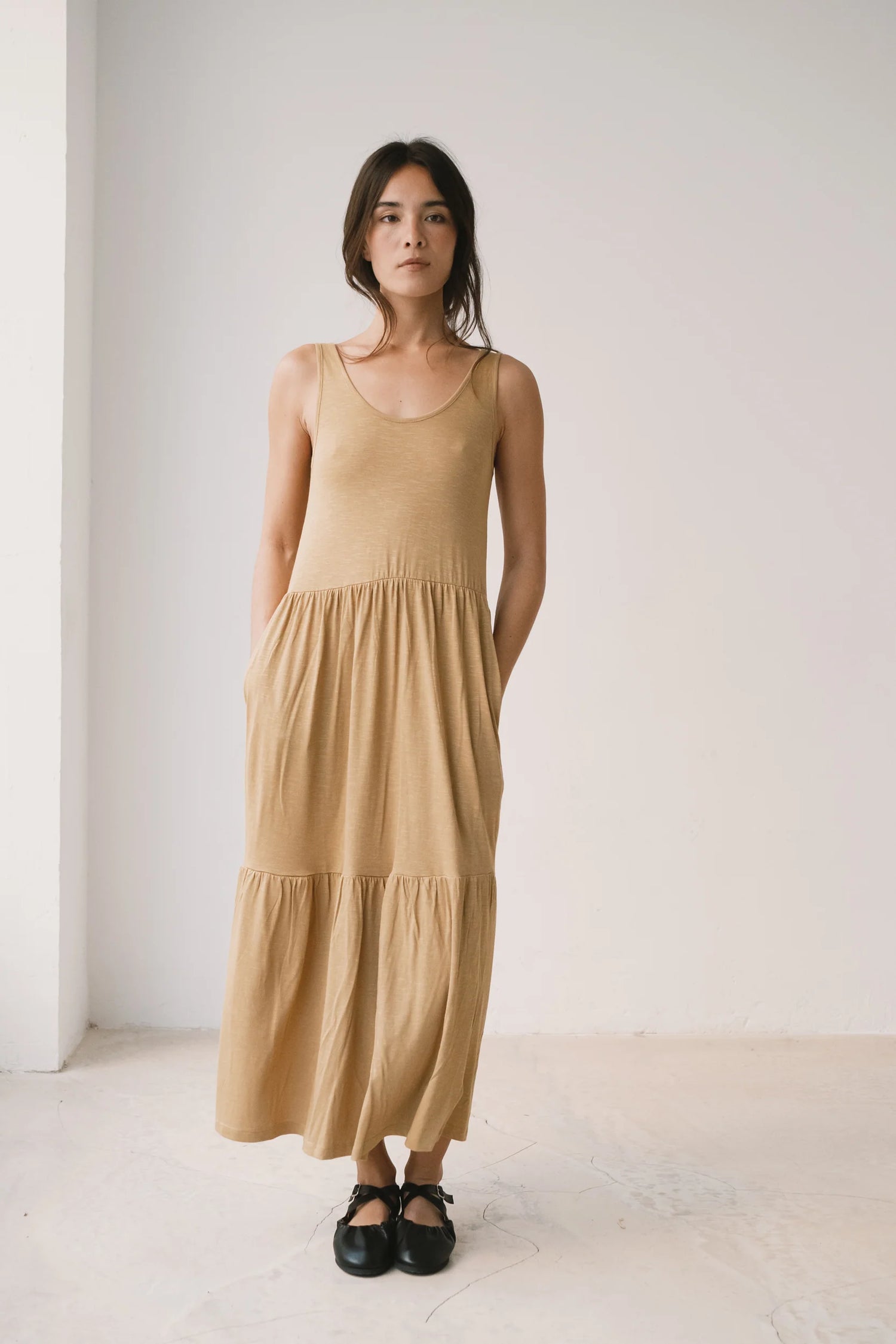 Woman wearing a beige dress standing against a white wall