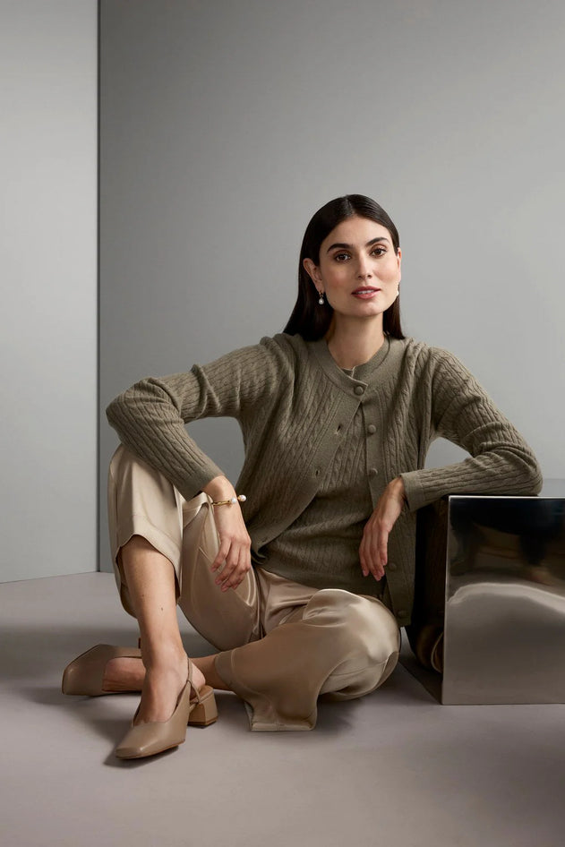 Woman sitting on a metallic cube wearing a brown sweater and beige pants against a gray background