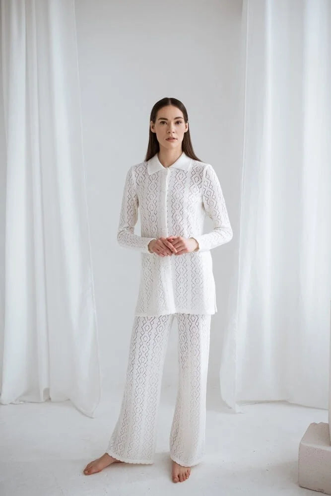 Woman wearing a white lace outfit standing against a white curtain.