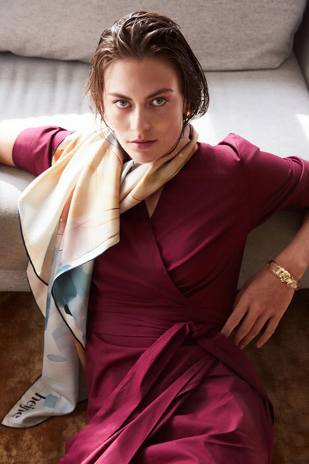 Woman in a burgundy dress with a colorful scarf sitting on a couch.
