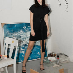 Person wearing a black dress standing in an art studio with a blue abstract painting in the background.