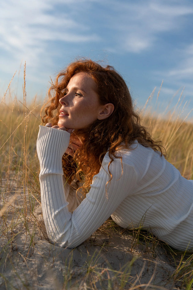 Woman lying on sand with grasses and blue sky in the background