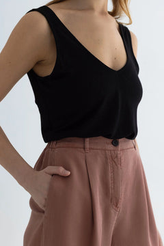 Person wearing a black sleeveless top and pink pants on a white background