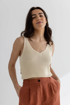 Woman wearing a beige ribbed tank top and rust-colored pants against a white background