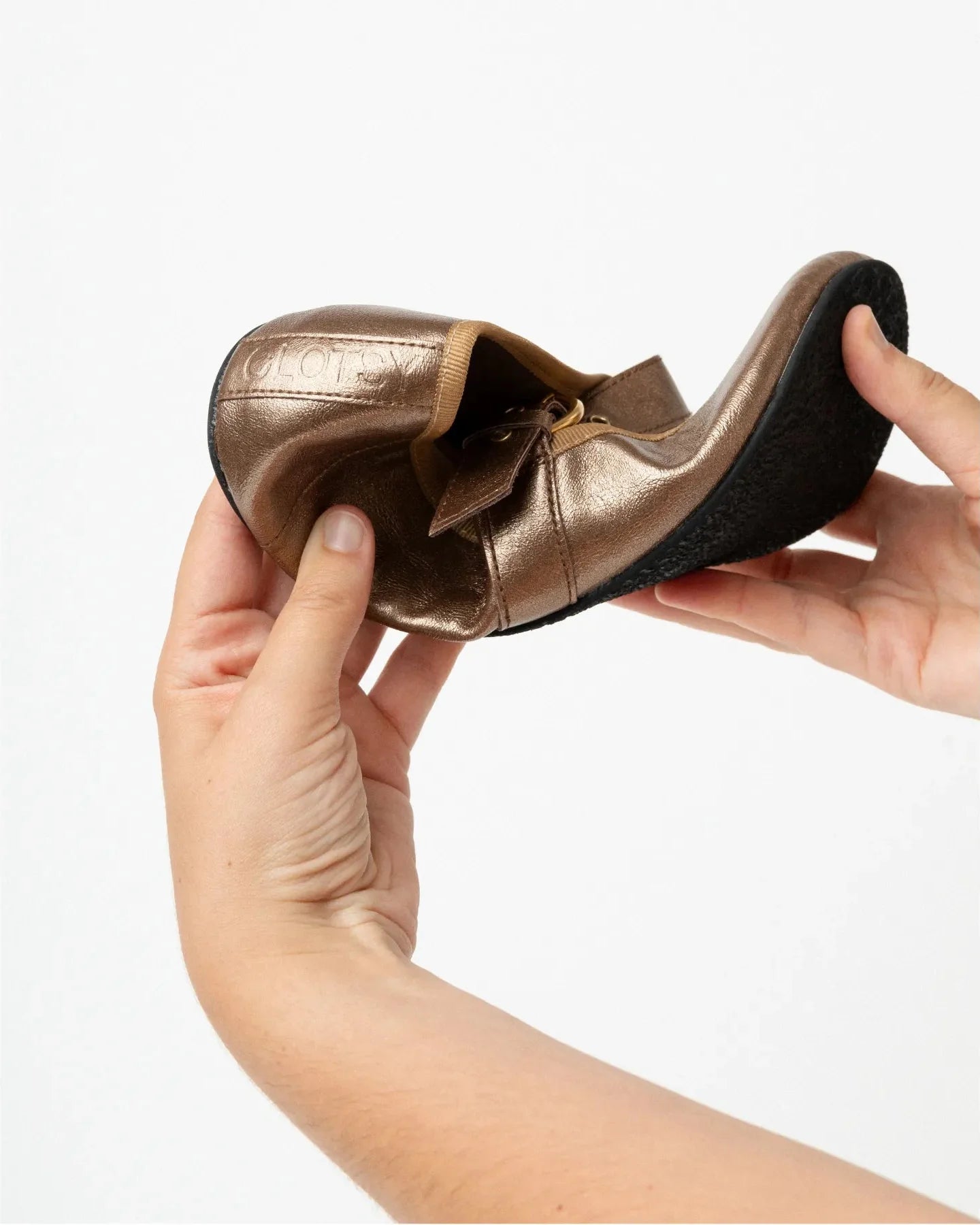 Gold ballet shoe held by a hand against a white background