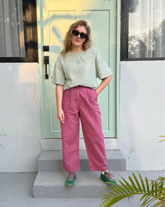 Person wearing a light green shirt and pink pants standing in front of a white door with a yellow frame.