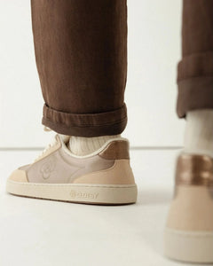 Beige sneakers worn with brown pants and white socks on a light background