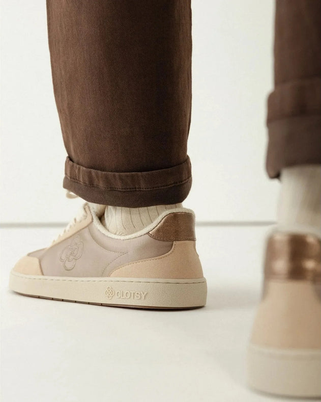 Beige sneakers worn with brown pants and white socks on a light background
