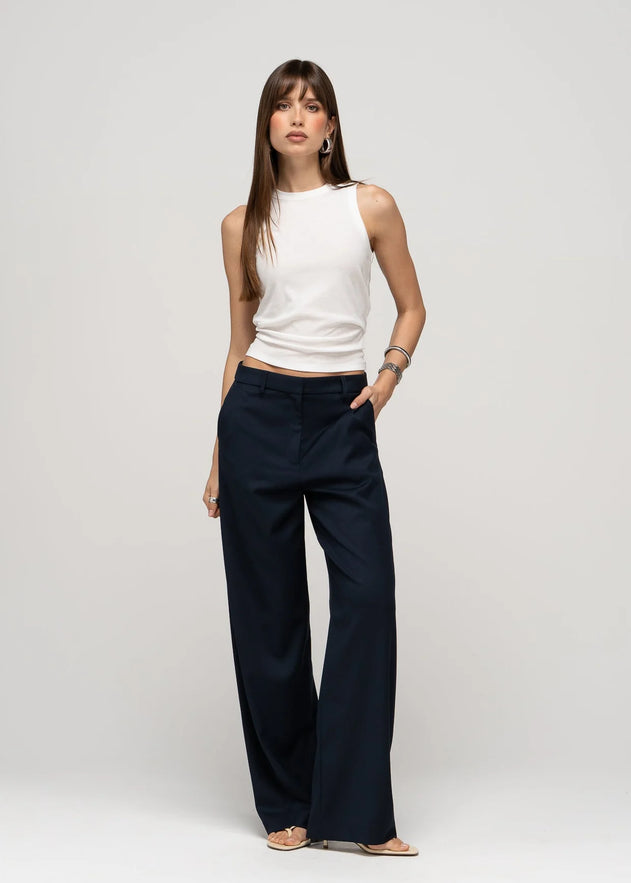 Woman wearing a white sleeveless top and navy wide-leg pants on a light gray background