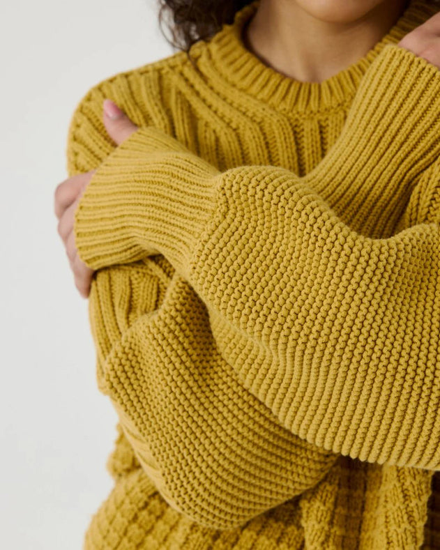 Close-up of a person wearing a mustard yellow knitted sweater on a white background