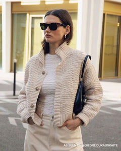 Woman wearing a beige knitted cardigan, white top, and beige pants on a city street.