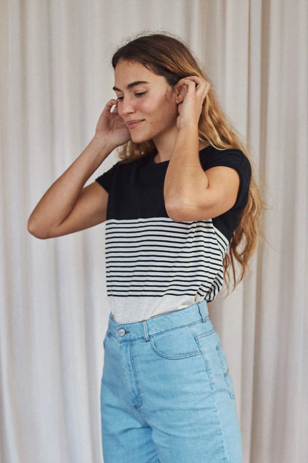 Woman wearing a black and white striped shirt with blue jeans against a neutral background