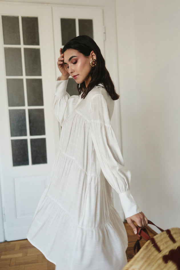 Woman in a white dress standing indoors with a neutral background