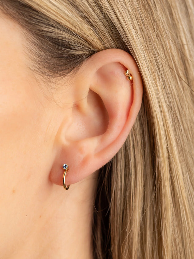 Close-up of an ear wearing a gold hoop earring with a blue gemstone.