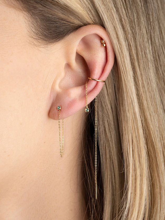 Close-up of a person's ear wearing gold earrings with green gemstones.