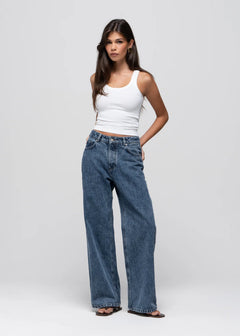 Woman wearing a white tank top and blue jeans on a light gray background