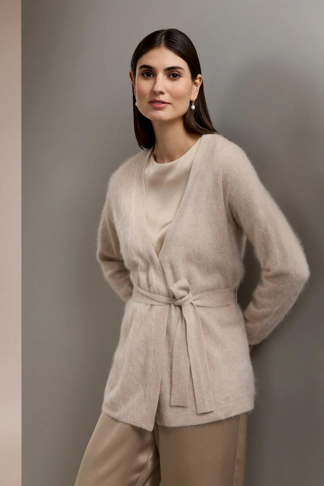 Woman wearing a beige belted cardigan and pants against a gray background