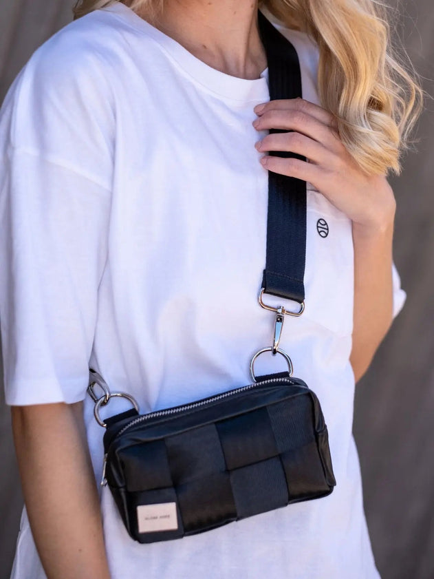 Person wearing a black woven handbag with a strap over the shoulder against a neutral background